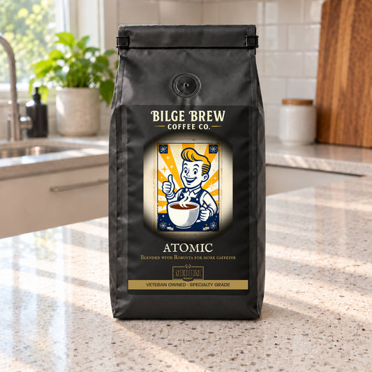 A black bag of Bilge Brew Coffee Co. Atomic blend coffee sits on a light speckled kitchen countertop with a blurred kitchen background.
