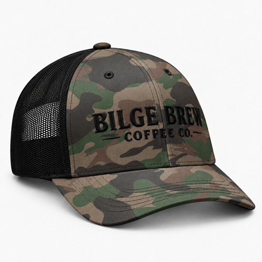 A camouflage trucker cap with black mesh back panels and black embroidered text reading 'BILGE BREW COFFEE CO.' on the front, shown on a clean white background.