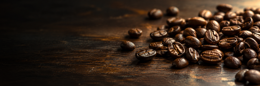 Dark roasted coffee beans scattered on a rustic dark wooden surface, with a warm spotlight highlighting the beans on the right side.