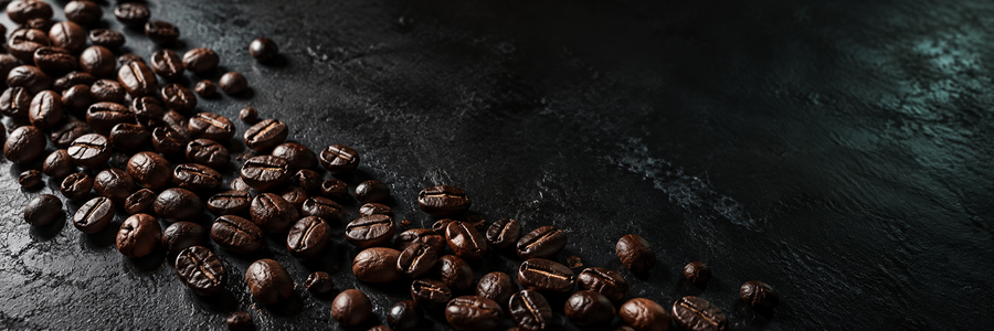 Roasted coffee beans scattered diagonally across a dark, textured black surface.