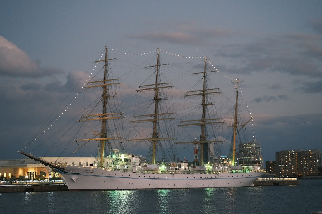 Tall ship illuminated at dusk with city lights in background