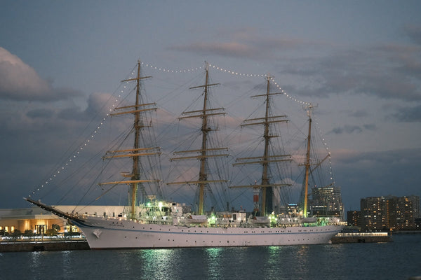 Tall ship illuminated at dusk with city lights in background