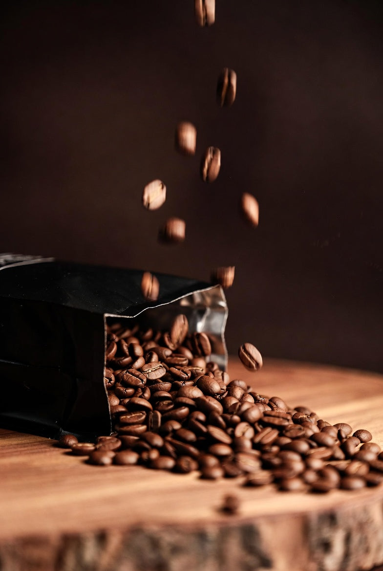 Roasted coffee beans spilling out of a black container on a wooden surface.