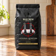 A black coffee bag from Bilge Brew Coffee Co. standing on a wooden table in a kitchen setting.
