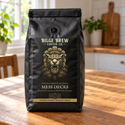 A black coffee bag from Bilge Brew Coffee Co. stands on a wooden table in a bright kitchen setting.