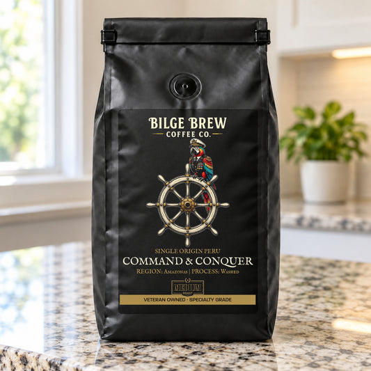 A black coffee bag labeled Bilge Brew Coffee Co. Command & Conquer, standing on a granite countertop in a kitchen setting.