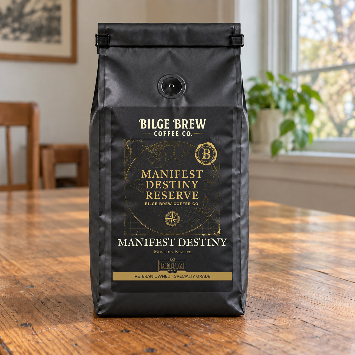 A black coffee bag labeled Bilge Brew Coffee Co. Manifest Destiny Reserve, standing on a wooden table in a softly lit indoor setting with a window and plant in the background.