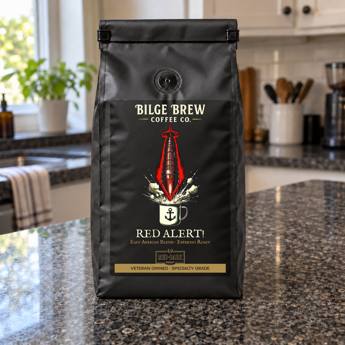 A black coffee bag labeled 'Bilge Brew Coffee Co. Red Alert!' stands on a granite kitchen countertop with a blurred kitchen background.