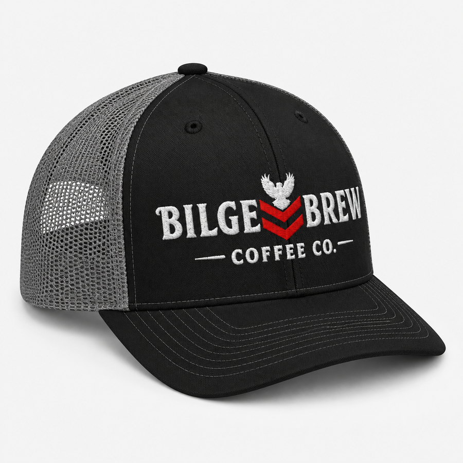 A black trucker hat with a gray mesh back, featuring a white embroidered eagle logo and the text 'BILGE BREW COFFEE CO.' with a red chevron accent on the front panel.