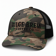 A camouflage trucker hat with black mesh back panels and black embroidered text reading 'BILGE BREW COFFEE CO.' on the front, shown on a clean white background.