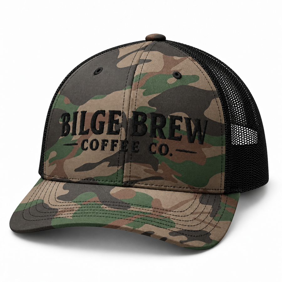 A camouflage trucker hat with black mesh back panels and black embroidered text reading 'BILGE BREW COFFEE CO.' on the front, shown on a clean white background.