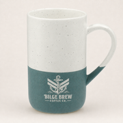 A ceramic coffee mug with a two-tone design, featuring a speckled white upper half and a dark teal lower half with a white printed anchor logo and the text 'BILGE BREW COFFEE CO.' The handle is white and the mug is photographed against a plain, light beige background.