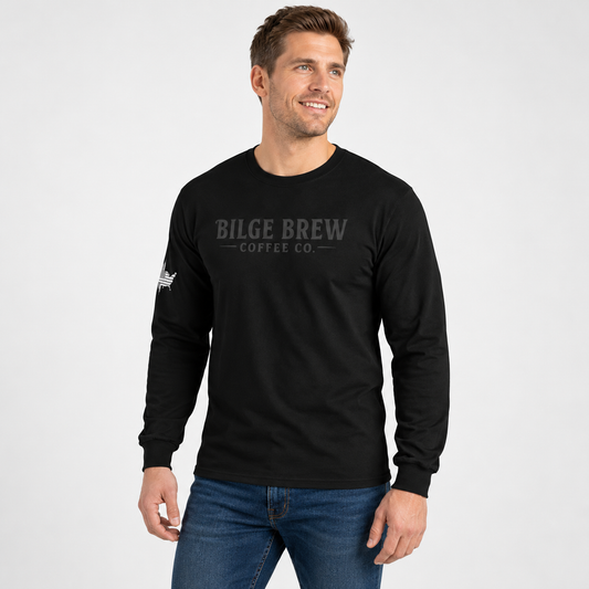 A man wearing a black long-sleeve t-shirt with 'BILGE BREW COFFEE CO.' printed in gray across the chest, paired with blue jeans, against a light gray studio background.