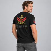 A man wearing a black short-sleeve t-shirt with a large graphic on the back, shown from a three-quarters back view against a light gray studio background. The graphic features a gold anchor over red and gray stripes, with the text 'BILGE BREW COFFEE CO.
