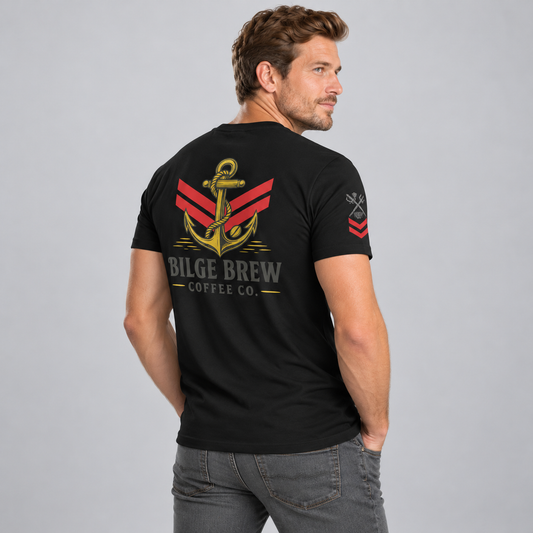 A man wearing a black short-sleeve t-shirt with a large graphic on the back, shown from a three-quarters back view against a light gray studio background. The graphic features a gold anchor over red and gray stripes, with the text 'BILGE BREW COFFEE CO.