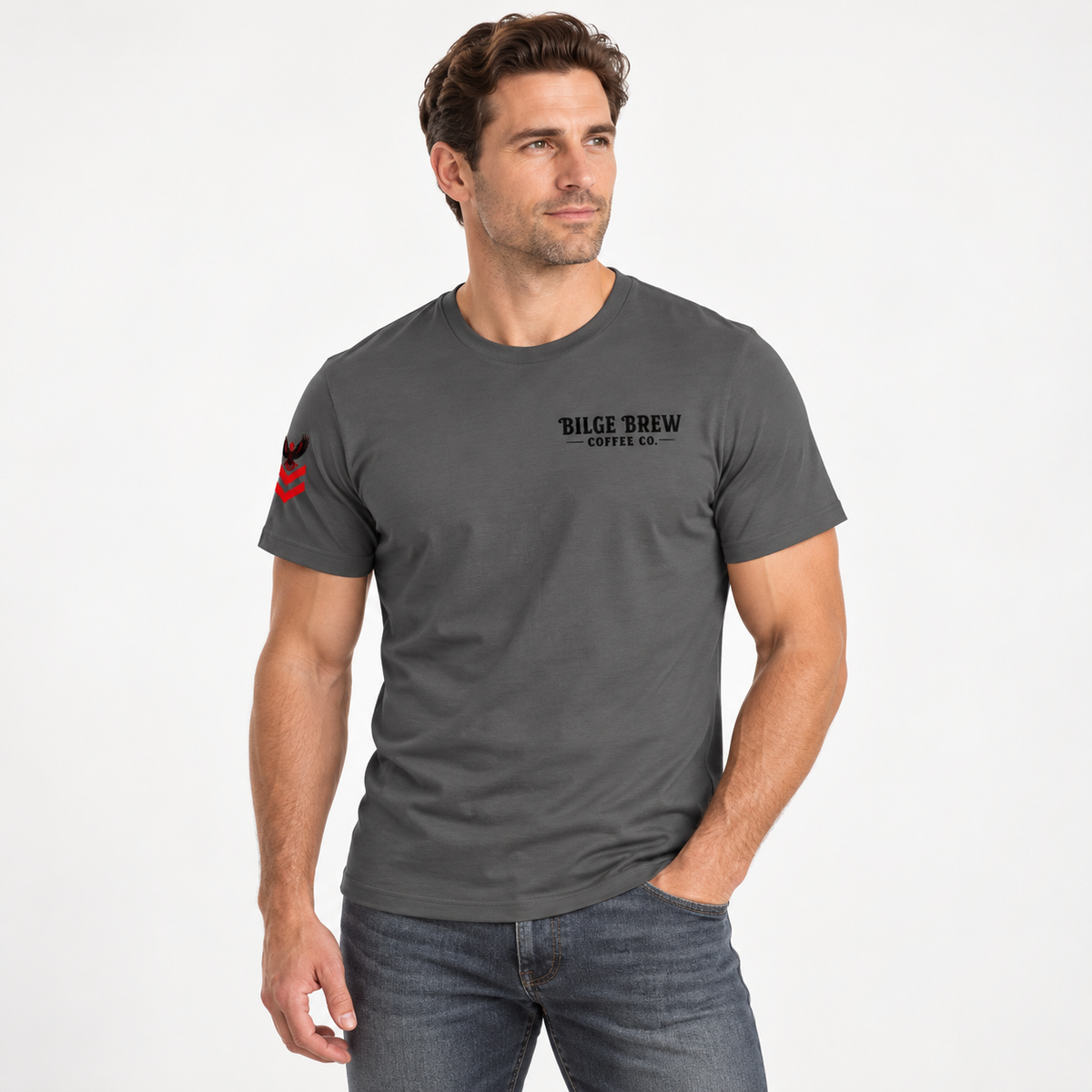 A man wearing a dark gray crewneck t-shirt with 'BILGE BREW COFFEE CO.' printed in black on the left chest and a small red graphic on the right sleeve, paired with blue jeans against a plain white background.