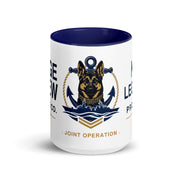 A white ceramic mug with a dark navy blue interior and rim, featuring a printed graphic of a German Shepherd dog with an anchor and rope emblem, and partial navy and gold text on a white background.