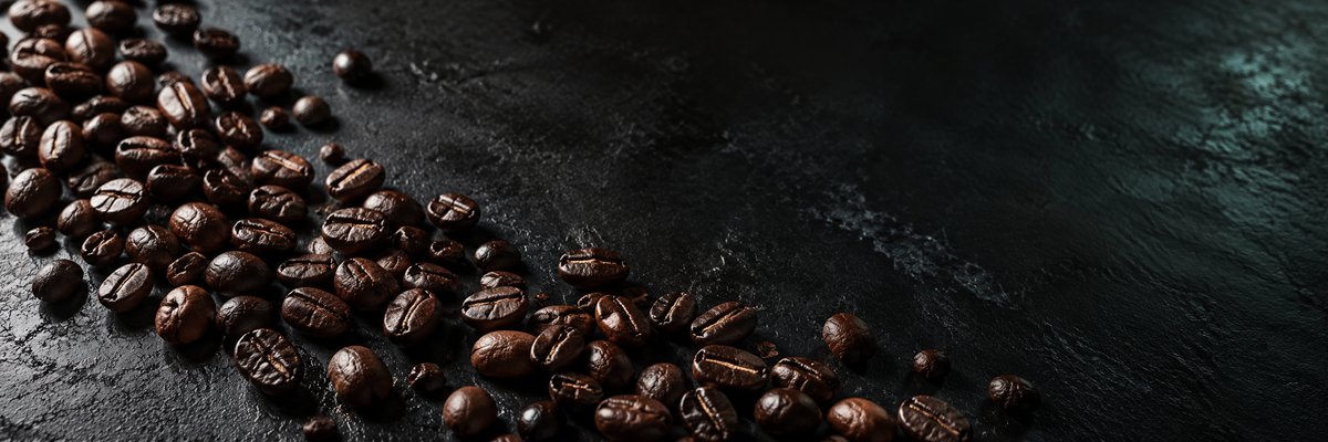 Roasted coffee beans scattered diagonally across a dark, textured black surface.