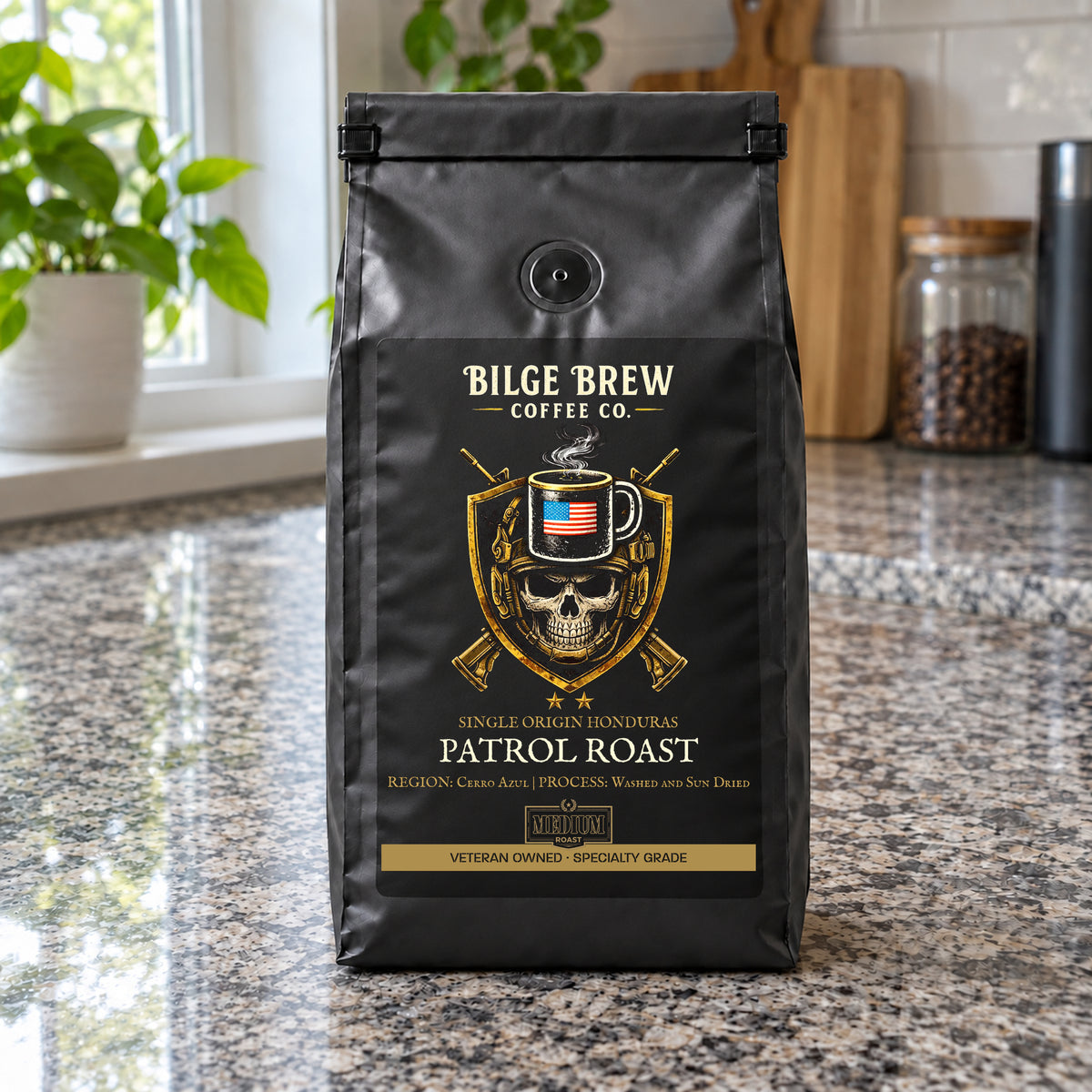 A black coffee bag labeled Bilge Brew Coffee Co. Patrol Roast stands on a granite kitchen counter with plants and jars blurred in the background.