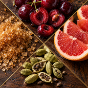 A close-up collage of food ingredients on a dark wooden surface: glossy dark red cherries, sliced pink grapefruit, coarse brown sugar, and green cardamom pods with seeds.