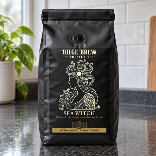 A black coffee bag labeled 'Bilge Brew Coffee Co. Sea Witch' stands on a dark countertop in a kitchen setting with a tiled wall and a plant in the background.