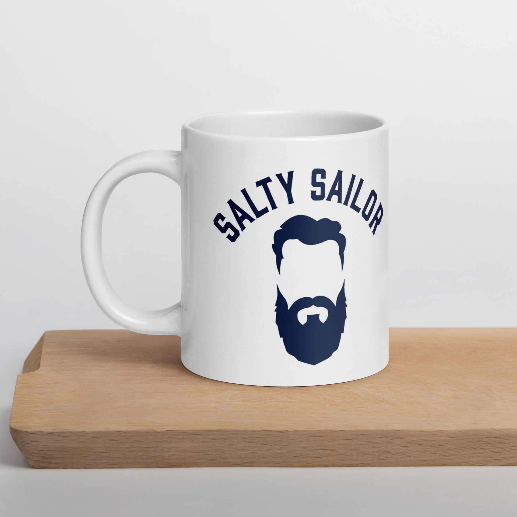 White mug with 'Salty Sailor' design featuring a beard illustration on a wooden surface.